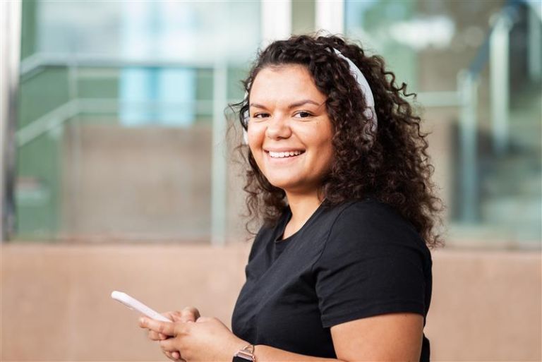 A young First Nations woman smiling while holding her phone