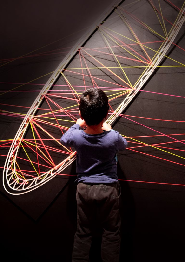 Child has back to camera and is interacting with weaving on wall