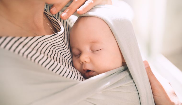 A mother carrying a baby in a sling in green mint colour