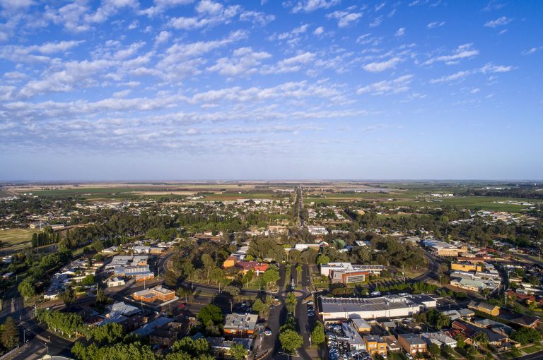 an aerial photo of a country town (Griffith in NSW). Buildings are laid out in a circle and there are roads and trees around the buildings. The sky is blue and has lots of wispy white clouds