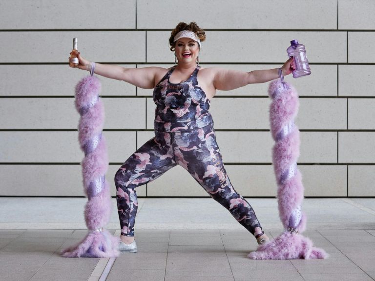 A woman wearing pink and grey active wear, smiling at the camera, standing in warrior pose.