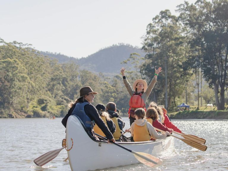 A lady standing in a 14 seater white canoe with her hands in the air