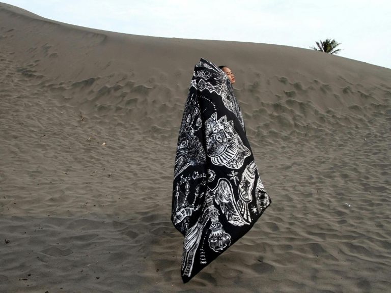 Female standing draped in batik print material on a sand dune