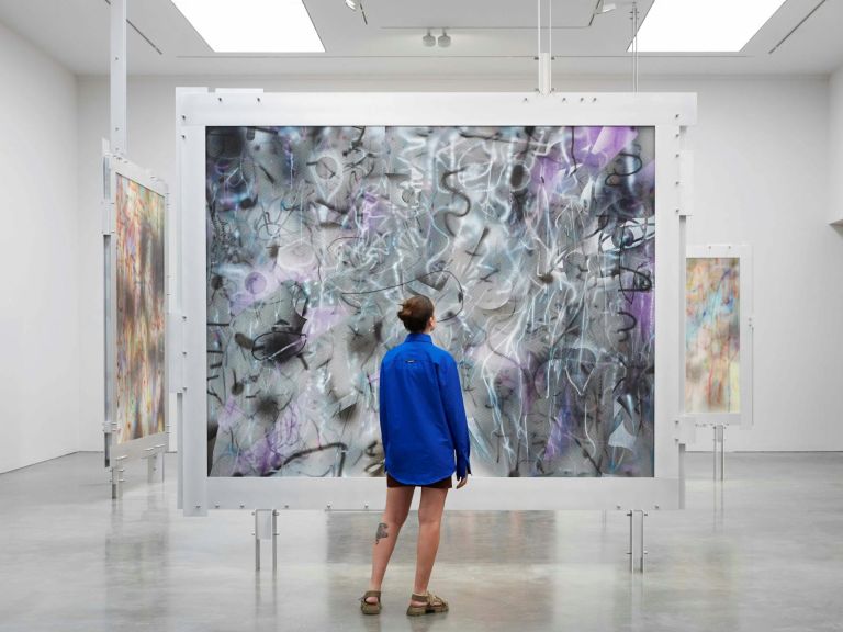 woman in bright blue shirt standing in gallery with concrete floor looking up at large-scale artwork