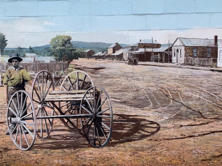 Painted image of 1880's Monero Street Queanbeyan featuring old buildings and a man with his cart