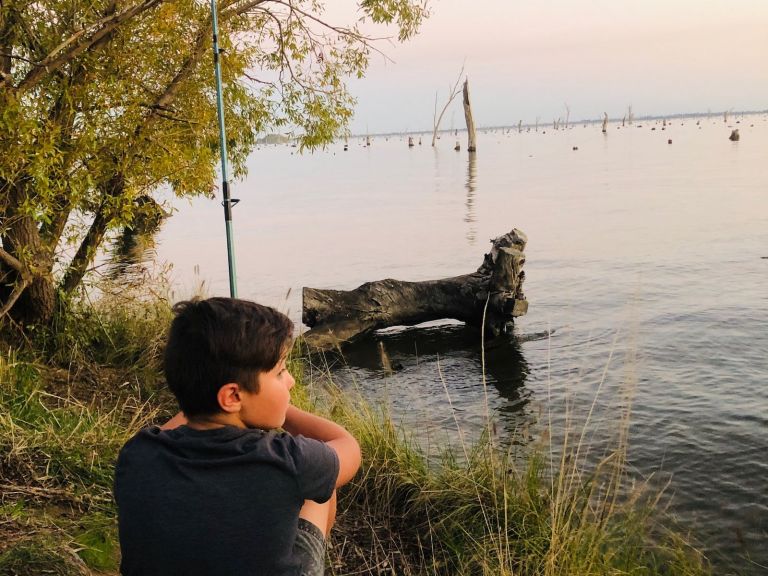 Young boy sitting watching the pink purple sunset of Lake Mulwala