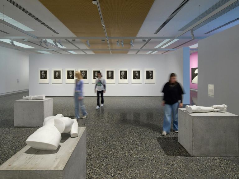 A gallery space with a A white sculpture of a man's upper body with no head or arms