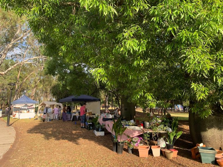 Several market stalls under green leafy trees