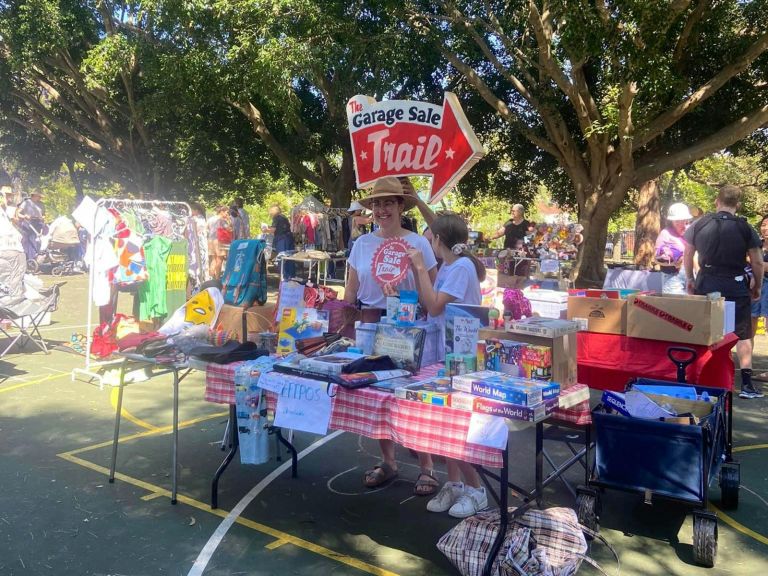 Outdoor market with table covered in assorted bric-a-brac and woman and child standing behind it