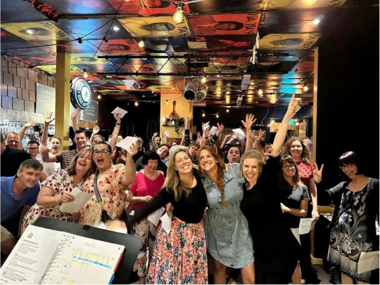 Group of people smiling and singing with their arms around each other