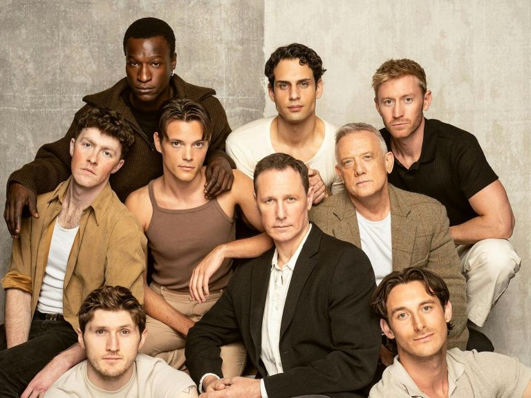 An all-male ensemble, sitting grouped together, all dressed in neutrals