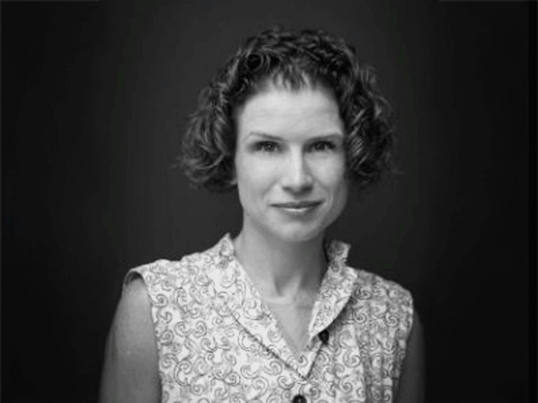 Black and white photo of woman with short curly hair looking at camera in sleeveless V-neck top