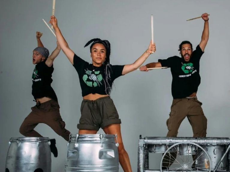 3 adult performers jumping in air while playing drums