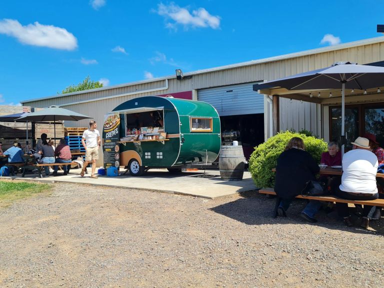 A Caravan with a Crepes sign with people sitting at a picnic table under umbrellas