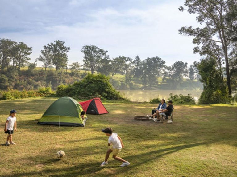 Parents sit outside their tent beside the Hawkesbury River while their kids play soccer, at Cattai