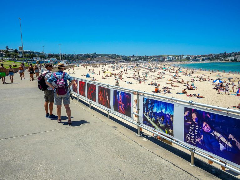 Two people looking at exhibitions hung along Bondi Beach Promenade