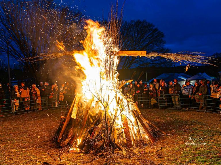 a large bonfire burning with a tall cross of sticks in the centre