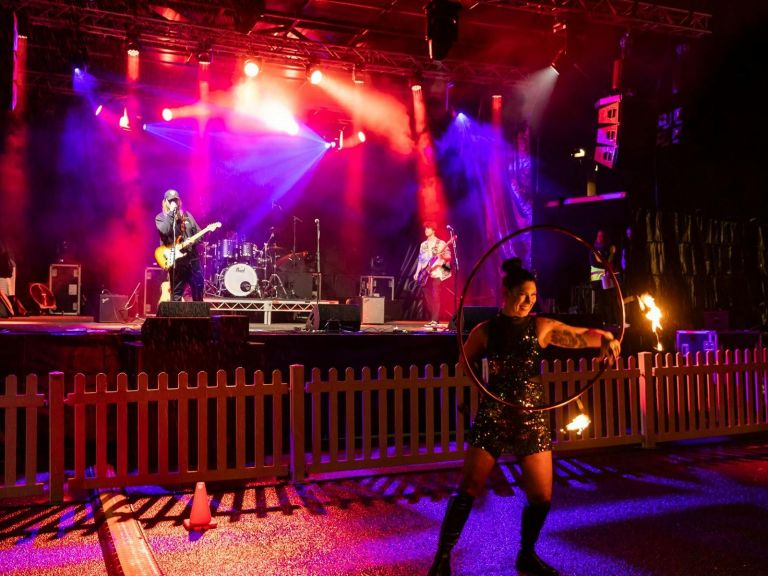 lady twirling a hoop in front of illuminated band stage, in the rain