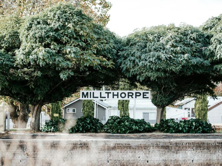 A train station platform with lush green trees says "Millthorpe"