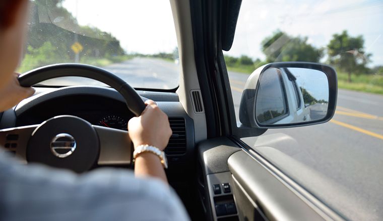 Drivers hand on steering wheel inside of a car driving and looking wing mirror women driving