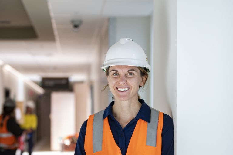 Jess Davis is standing on a construction site in hi-vis with a hard hat on.