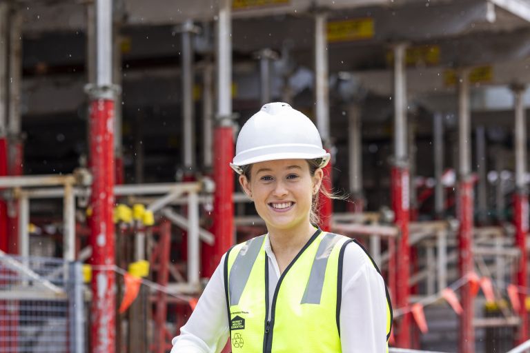 Sian is standing on a construction site wearing hi vis and a hard hat.