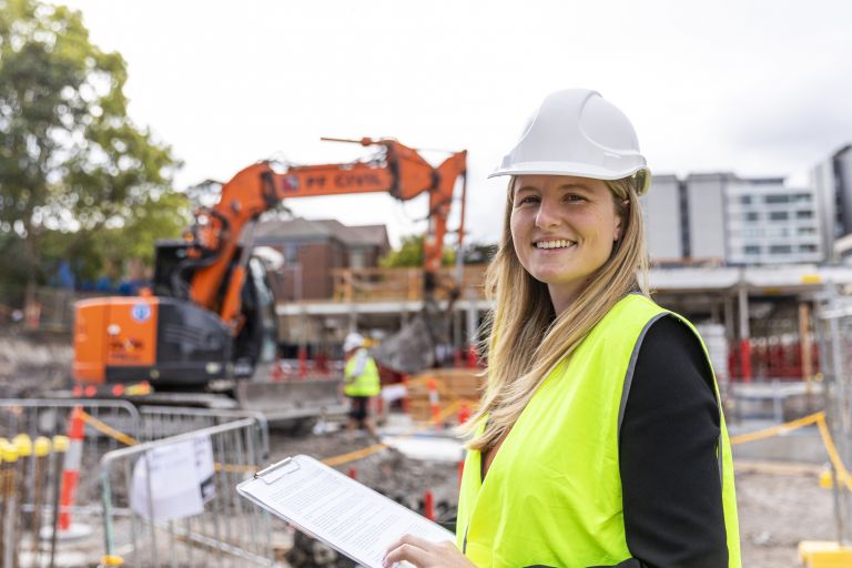 Woman on a construction site wearing hi-vis and wearing a hard hat.