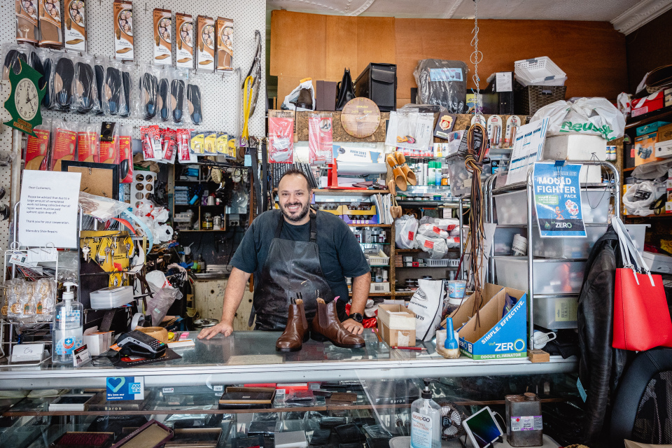 A male cobbler holding a leather boot behind a glass counter
