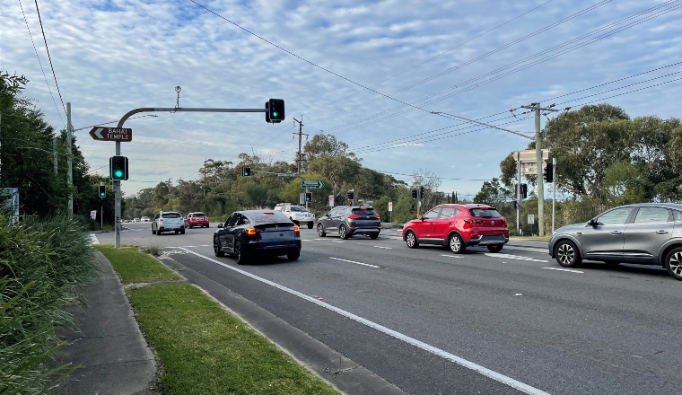 A busy intersection with traffic lights, cars, and a sign on a light pole that reads 'BAHAI TEMPLE'